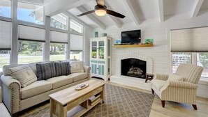 A living room with a sofa, armchair, fireplace, television, and ceiling fan.