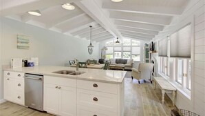 A spacious kitchen with a central island, white cabinetry, and a dishwasher. There is a dining area with a bench and a sofa.