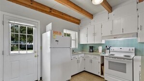 Una cocina con armarios blancos, un refrigerador, una estufa y una cafetera.