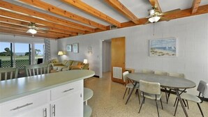 Una cocina amplia con una isla central, vigas de madera en el techo y un comedor con una mesa redonda y sillas.