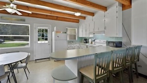 Una cocina con vigas de madera, armarios blancos, una isla central con sillas y una mesa de comedor.