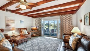 A spacious living room with a high ceiling, wooden beams, a patterned rug, leather sofas, a television, and a view through large glass doors. - Bill Smith House B - great location with ocean views (Jekyll Island)