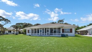 A single-story house with a covered porch, a well-maintained lawn, and a clear blue sky. - Bill Smith House B - great location with ocean views (Jekyll Island)