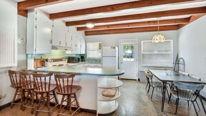 A kitchen with wooden beams, white cabinets, a central island with stools, and a dining table with chairs. - Bill Smith House B - great location with ocean views (Jekyll Island)