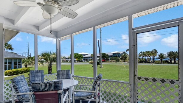 A covered outdoor area with a table and chairs, large windows, and a view of a green lawn and buildings. - Bill Smith House B - great location with ocean views (Jekyll Island)