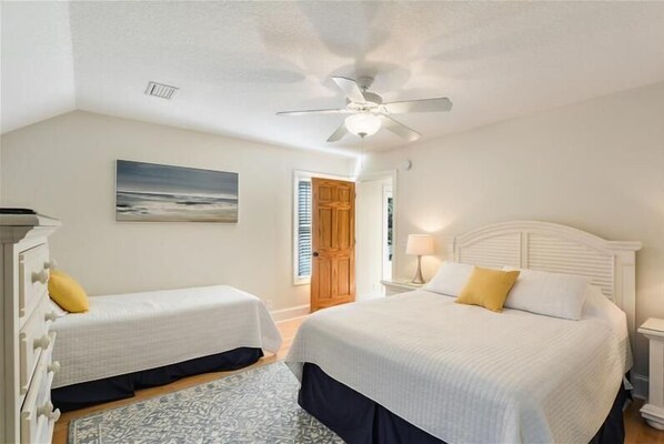 A bedroom with two beds, a ceiling fan, a painting, and a door.