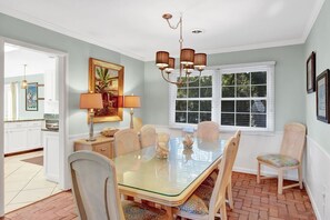 Comedor con mesa de vidrio, seis sillas, candelabro y ventana con persianas.