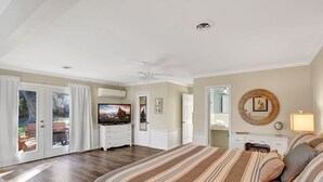 Een slaapkamer met een groot bed, een televisie, een plafondventilator en uitzicht door de glazen deuren.