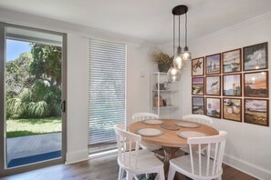Un coin repas avec une table ronde, des chaises blanches et une vue sur l’extérieur grâce à une porte-fenêtre coulissante.
