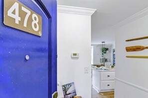 Quarto com porta azul identificada com o número '478', termostato, área de cozinha com armários brancos e boias de madeira na parede.