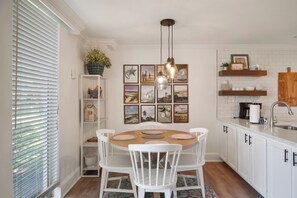 Une cuisine avec des meubles blancs, une table de salle à manger ronde entourée de chaises blanches et un luminaire suspendu.