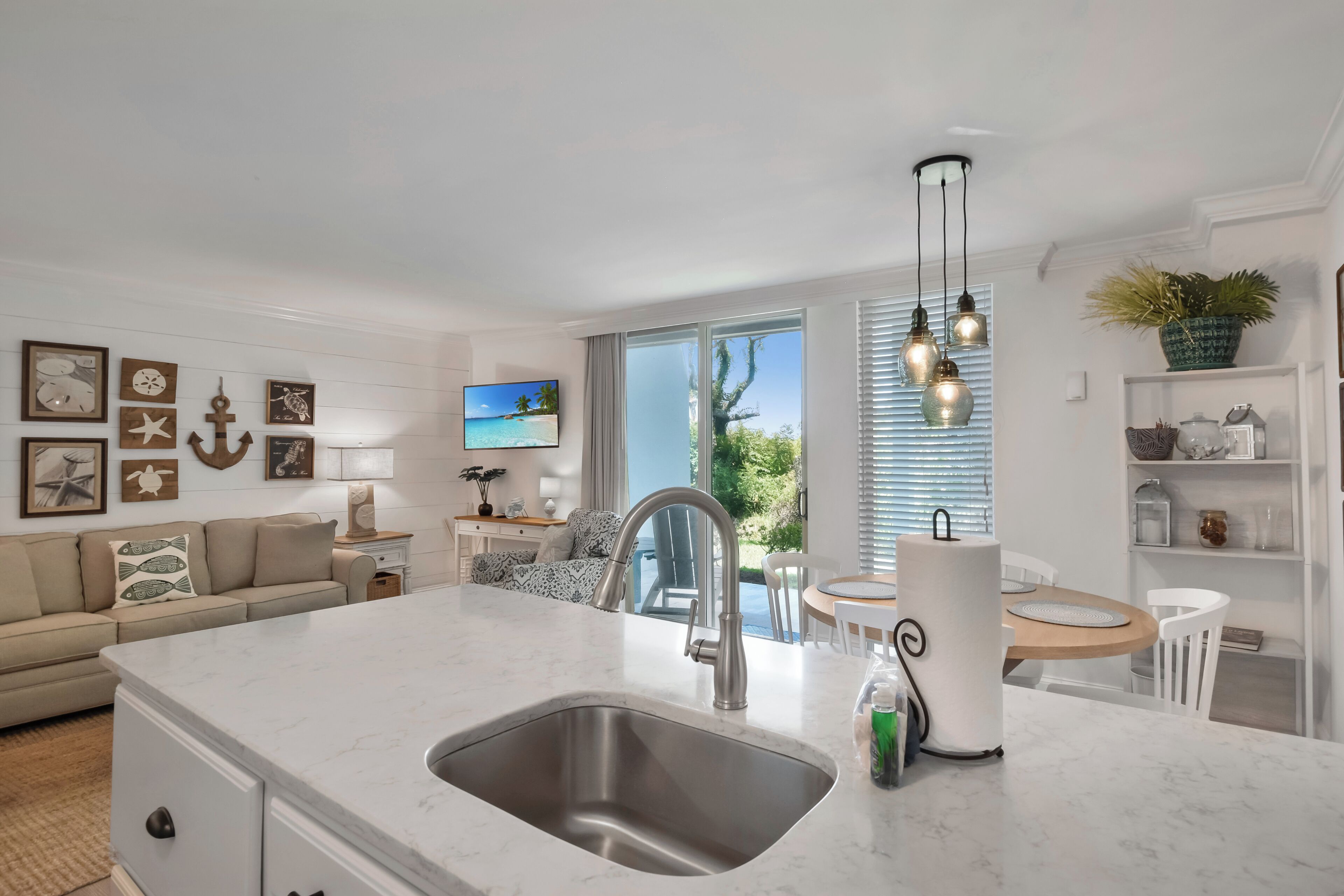 A modern kitchen with a large island, stainless steel sink, and pendant lighting.