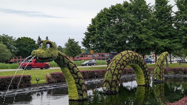 A pond with two large, arching structures resembling animals, surrounded by a well-maintained garden and a building in the background. - MAgog~Condo C.O.Z.Y. Cocooning ~ Lake Memphré (Magog)