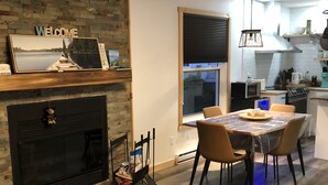 A modern kitchen with a fireplace, dining table, and chairs. - MAgog~Condo C.O.Z.Y. Cocooning ~ Lake Memphré (Magog)