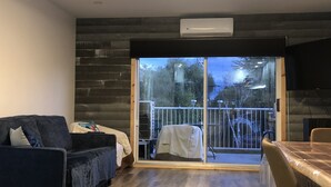 A modern living room with a dark blue sofa, a wooden floor, and a large sliding glass door leading to a balcony with a metal railing. - MAgog~Condo C.O.Z.Y. Cocooning ~ Lake Memphré (Magog)