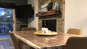 A dining area with a covered table, chairs, a fireplace, a TV, and a balcony. - MAgog~Condo C.O.Z.Y. Cocooning ~ Lake Memphré (Magog)