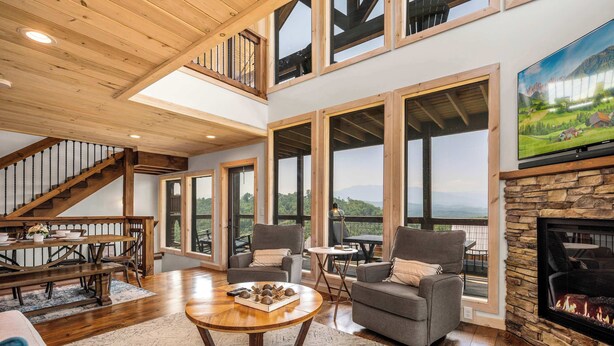 A spacious living room with a fireplace, large windows, and a staircase leading to an upper level. - Spectacular View 3 Bd Luxury Smoky Mountain Cabin (Sevierville)