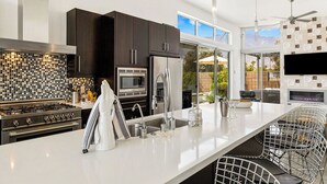 A modern kitchen with dark cabinets, a stainless steel refrigerator, a microwave, and a gas stove. - Troubadour - Mid Mod Getaway (Palm Springs)