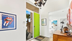 A hallway with a framed Rolling Stones poster, a green door, a dining area with a table and chairs, and a chandelier. - Troubadour - Mid Mod Getaway (Palm Springs)