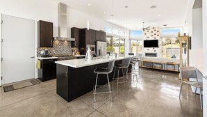 A modern kitchen with a large island, bar stools, and a built-in TV. - Troubadour - Mid Mod Getaway (Palm Springs)