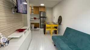Una sala de estar moderna con un sofá color turquesa, un mueble blanco para televisión y una mesa de comedor amarilla con sillas.