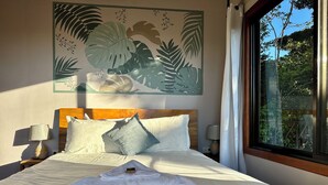 A neatly made bed with a folded towel, a wooden headboard, and a wall art of tropical leaves. - Wake Up with Birds in Monteverde - Forest Balcony & Walk to Reserves (Monteverde)