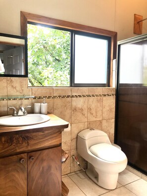 A bathroom with a wooden vanity, a white sink, a toilet, and a window with a view of greenery. - Wake Up with Birds in Monteverde - Forest Balcony & Walk to Reserves (Monteverde)