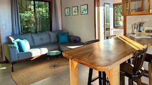 A living room with a sofa, a dining table, and a kitchen area with cabinets. - Wake Up with Birds in Monteverde - Forest Balcony & Walk to Reserves (Monteverde)