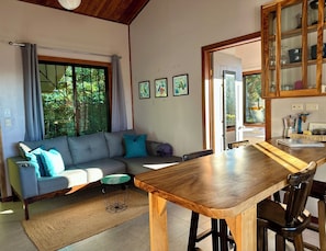 A living room with a sofa, a dining table, and a kitchen area with cabinets.