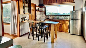 A kitchen with wooden cabinets, a stainless steel refrigerator, and a large window. - Wake Up with Birds in Monteverde - Forest Balcony & Walk to Reserves (Monteverde)