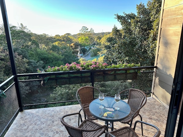 A balcony with wicker chairs, a glass table, and two wine glasses.