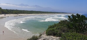 A beach with clear waters, a sandy shore, and a mountainous backdrop. - Great location! House 5 minutes walk from Praia da Enseada. We accept pets!! (Bertioga)