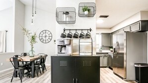 A modern kitchen with a central island, stainless steel appliances, and a dining area with a wooden table and chairs. - Industrial Chic South Lubbock 3/2 (Lubbock)