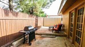 A backyard with a barbecue grill, a patio table with chairs, and a wooden fence. - Industrial Chic South Lubbock 3/2 (Lubbock)