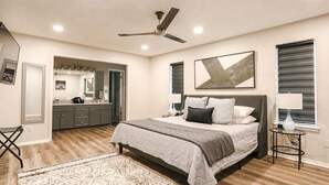 A bedroom with a bed, bedside tables, a ceiling fan, and a bathroom visible through an open door. - Industrial Chic South Lubbock 3/2 (Lubbock)