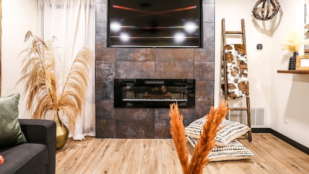 Een moderne woonkamer met een flatscreen televisie aan een stenen muur, een open haard onder en een houten vloer.