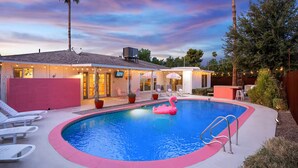 A swimming pool with a pink flamingo float, lounge chairs, and a covered patio area with string lights.