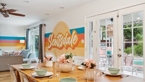 A dining area with a wooden table set for four, a large wall mural, and a view of the outdoors through glass doors.