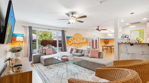 A modern living room with a sofa, coffee table, wicker chairs, and a dining area with chairs and a table.