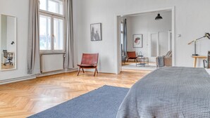 A spacious room with a large window, a wooden floor, a bed, a chair, and a desk with a lamp. - Hip Innere Stadt 3BR w/ Elevator, Best Location in Vienna, by Blueground (Vienna)