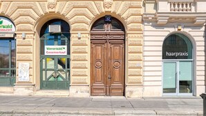 A building facade with a large wooden door, a sign for 'Wiemerwald Gassenverkauf', and a 'haarpraxis' sign. - Hip Innere Stadt 3BR w/ Elevator, Best Location in Vienna, by Blueground (Vienna)