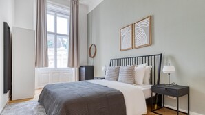 Et soveværelse med en seng, et natbord, en lampe og et billede på væggen.