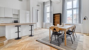 Et moderne køkken med hvide skabe, en træbordplade og en mikrobølgeovn. Der er et spiseområde med et bord og stole, et tæppe og en reol.