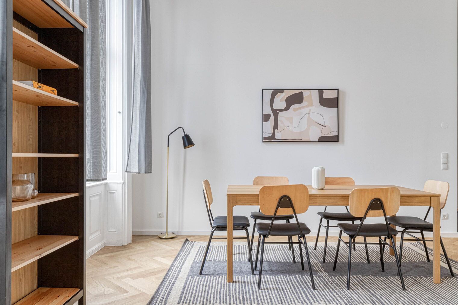 Un'area pranzo moderna con un tavolo e sedie in legno, una lampada da terra e un quadro appeso al muro.