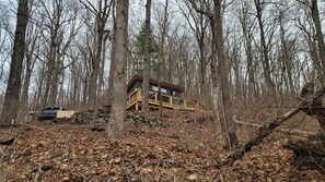 Una cabaña en un bosque con terraza de madera y base de piedra.