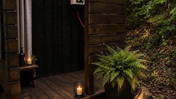 A wooden outdoor shower with a built-in heater, surrounded by rocks and pebbles, with a potted fern and candles for ambiance.