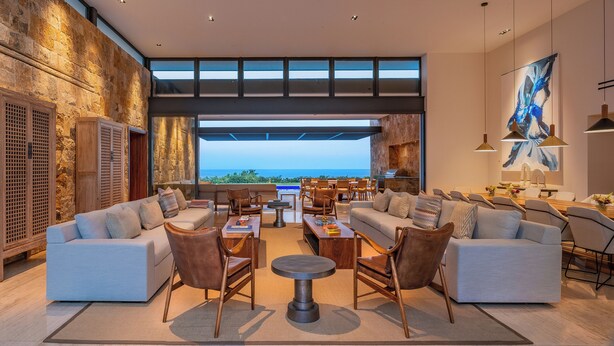 A spacious living area with a large window overlooking a scenic view, furnished with sofas, chairs, and a coffee table. - Stunning 11-Bd Villa, Indoor Tennis & Beach Club — Chef, Butler & Yacht Incl. (San Jose del Cabo)