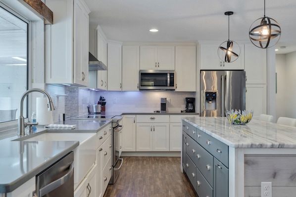 A modern kitchen with white cabinetry, stainless steel appliances, and a marble countertop.