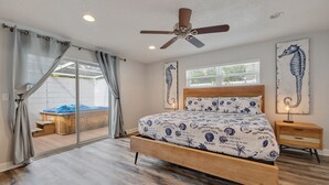 A bedroom with a wooden bed, a ceiling fan, and a view of a hot tub through a sliding glass door.