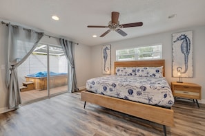 A bedroom with a wooden bed, a ceiling fan, and a view of a hot tub through a sliding glass door.